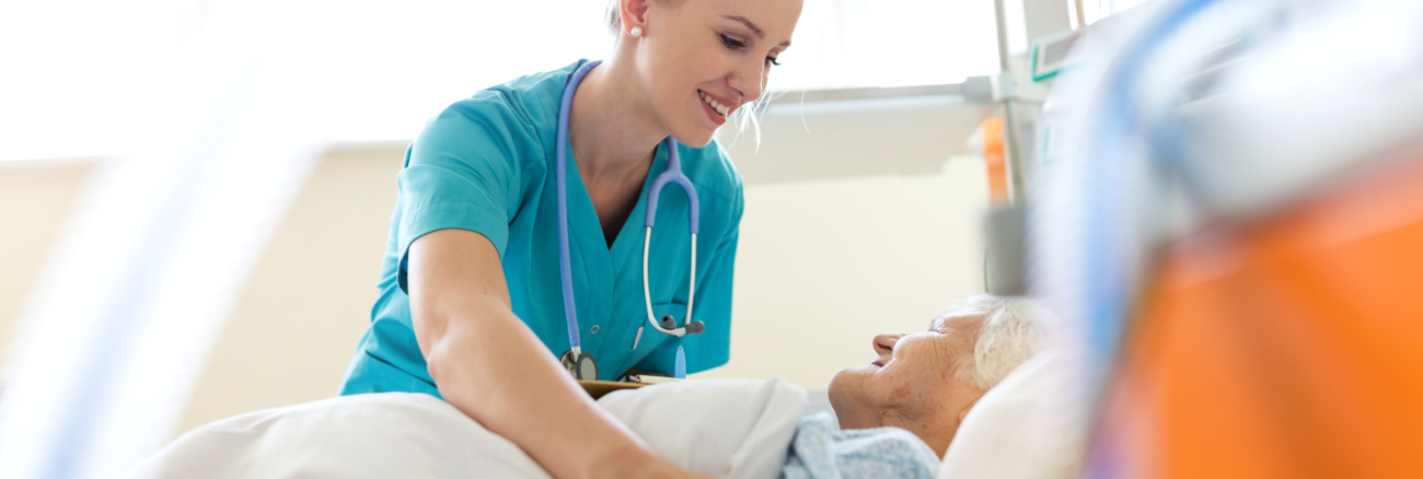 Eine Krankenschwester versorgt in einem Krankenhaus eine ältere Patientin, die im Bett liegt © iStock/PIKSEL