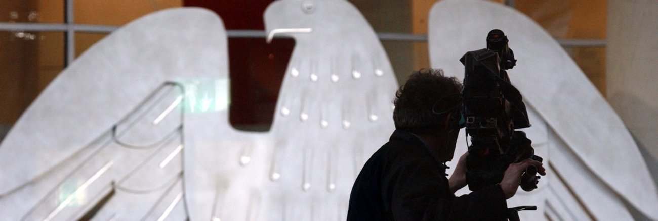 Silhouette eines Kameramanns mit Kamera vor dem Bundesadler im Plenarsaal des Bundestages © DBT/Hans-Günther Oed Silhouette eines Kameramanns mit Kamera vor dem Bundesadler im Plenarsaal des Bundestages © DBT/Hans-Günther Oed
