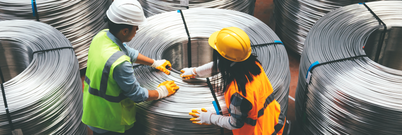 Eine Arbeiterin und ein Arbeiter in verpacken riesige Draht-Rollen © iStock/serts