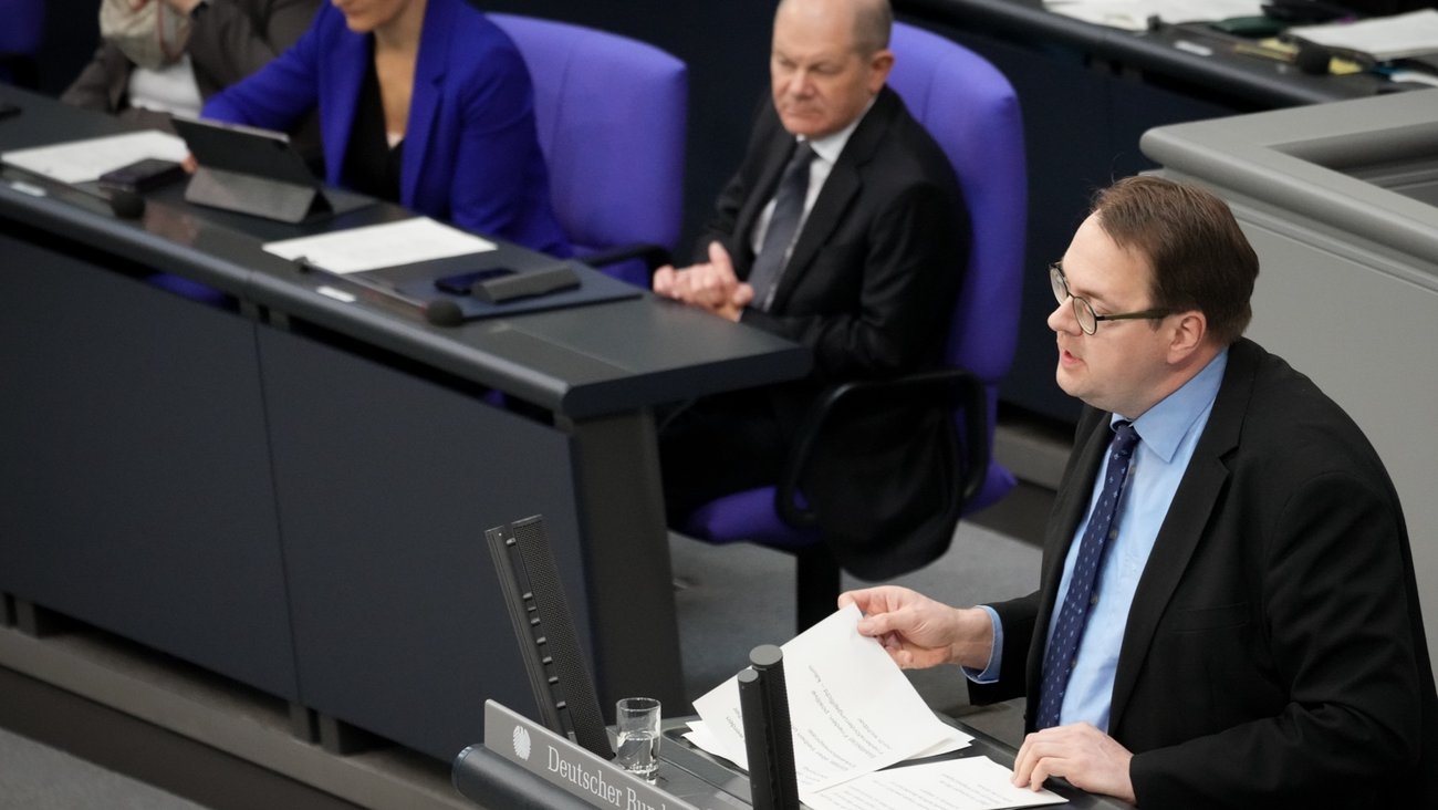 Sören Pellmann am Rednerpult des Bundestages, dahinter Bundeskanzler Olaf Scholz auf der Regierungsbank