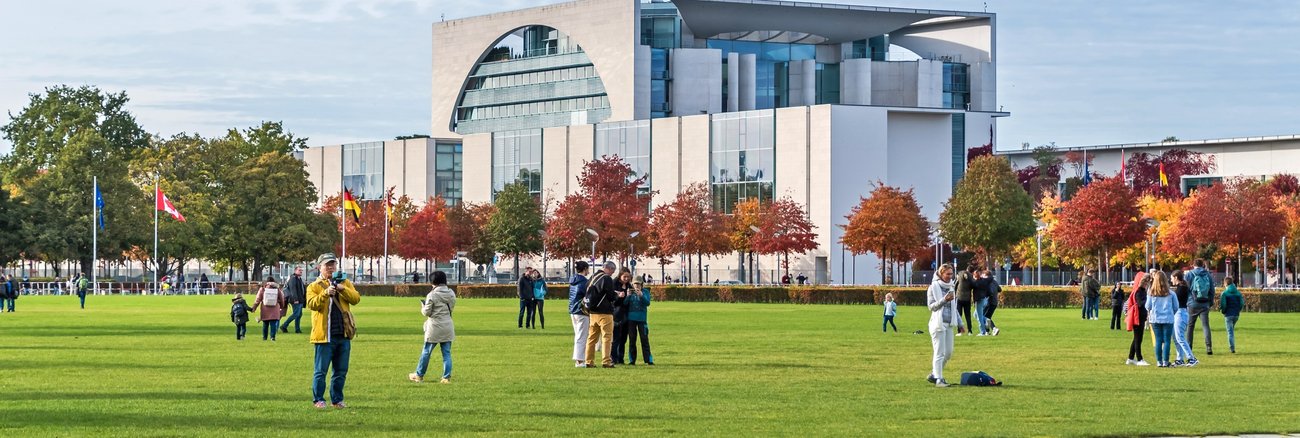 Menschen vor dem Bundeskanzleramt auf der Wiese des Platzes der Republik © iStock/laranik