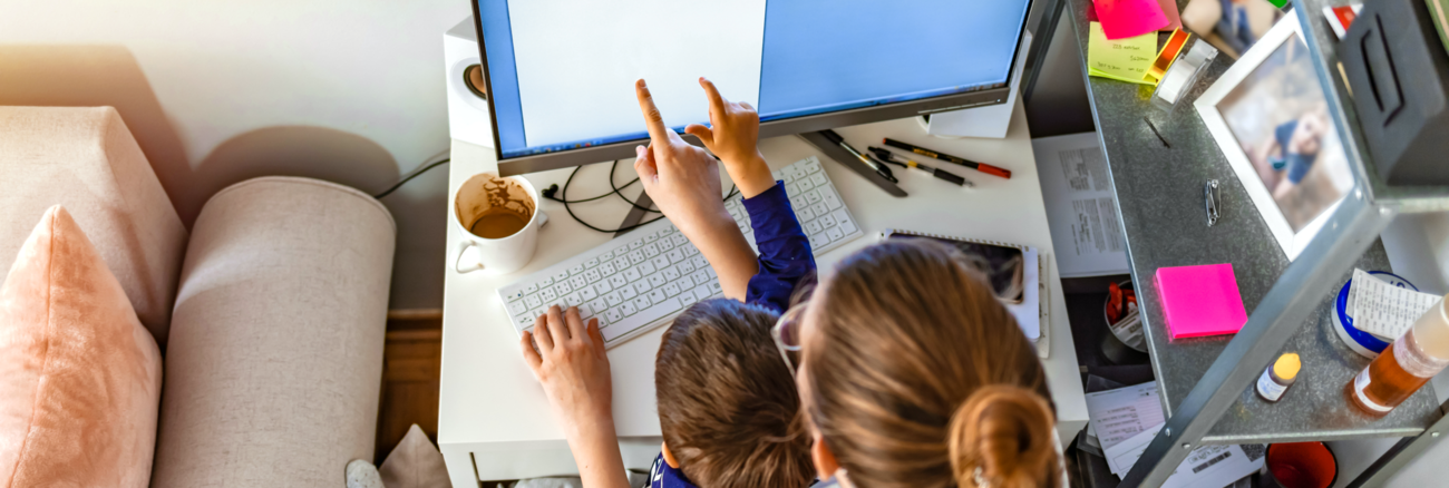 Eine Frau mit einem Kind auf dem Schoß zeigt auf einen Computerbildschirm © iStock/ljubaphoto