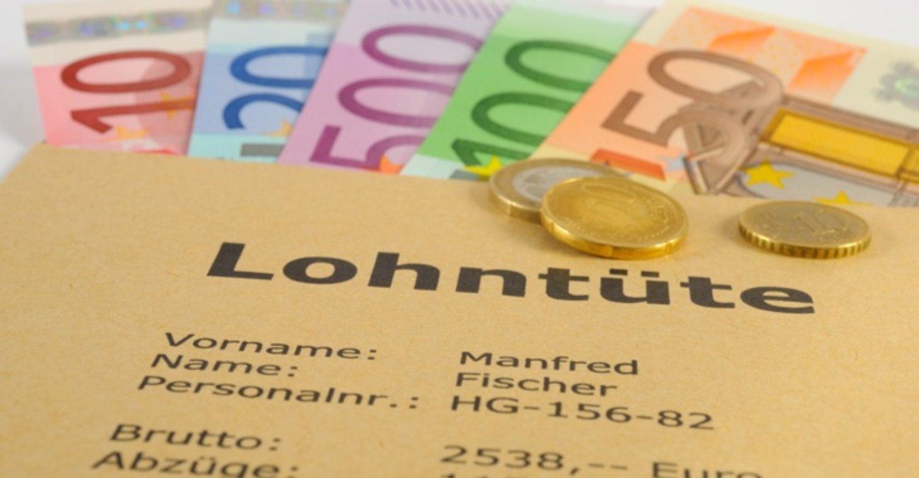 Euro-Münzen auf einem Umschlag mit der Aufschrift Lohntüte, darunter Euro-Scheine © iStock/filmfoto