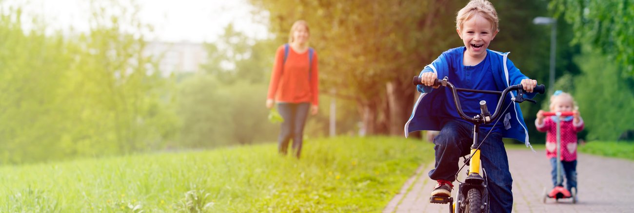 Eine Mutter mit ihrem Sohn auf einem Fahrrad und ihrer Tochter auf einem Tretroller © iStockphoto.com/Nadezhda1906