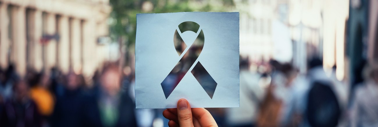 Verschwommene Menschengruppe hinter einer Red Ribbon-Schablone @iStock/Bulat Silvia Verschwommene Menschengruppe hinter einer Red Ribbon-Schablone @iStock/Bulat Silvia