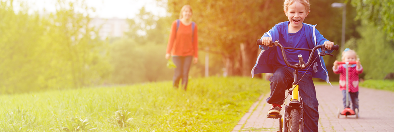 Ein Kind fährt lachend auf einem Fahrrad über einen Weg in einer Grünanlage. | Foto: © istock.com/Nadezhda1906 Ein Kind fährt lachend auf einem Fahrrad über einen Weg in einer Grünanlage. | Foto: © istock.com/Nadezhda1906