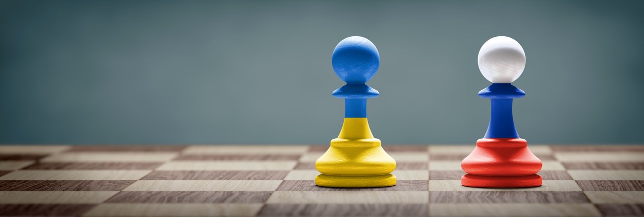 Zwei Schachfiguren in den Farben der Staatsflaggen der Ukraine und Russlands auf einem Schachbrett © iStock/ffikretow Zwei Schachfiguren in den Farben der Staatsflaggen der Ukraine und Russlands auf einem Schachbrett © iStock/ffikretow
