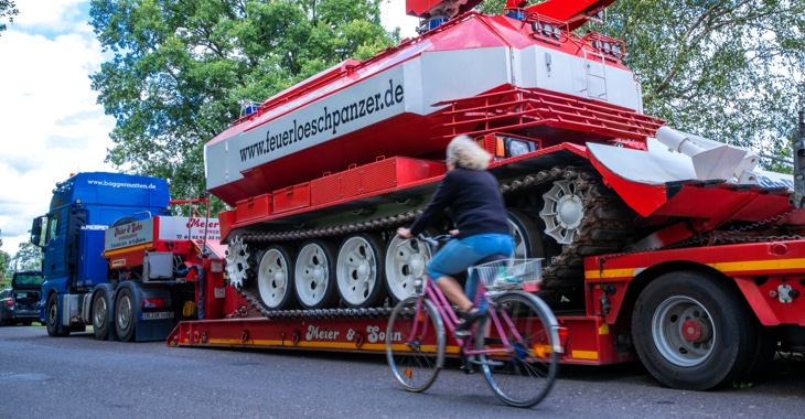 Waldbrand in Lübtheen in Mecklenburg-Vorpommern: Eine Frau fährt mit einem Fahrrad an einem Tieflader mit einem Feuerlöschpanzer vorbei © dpa/Jens Büttner Waldbrand in Lübtheen in Mecklenburg-Vorpommern: Eine Frau fährt mit einem Fahrrad an einem Tieflader mit einem Feuerlöschpanzer vorbei © dpa/Jens Büttner