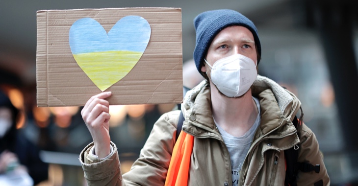 Ein Mann auf dem Berliner Hauptbahnhof hält ein Schild mit einem Herz in den Farben der ukrainischen Flagge. © picture alliance/SZ Photo|Jens Schicke