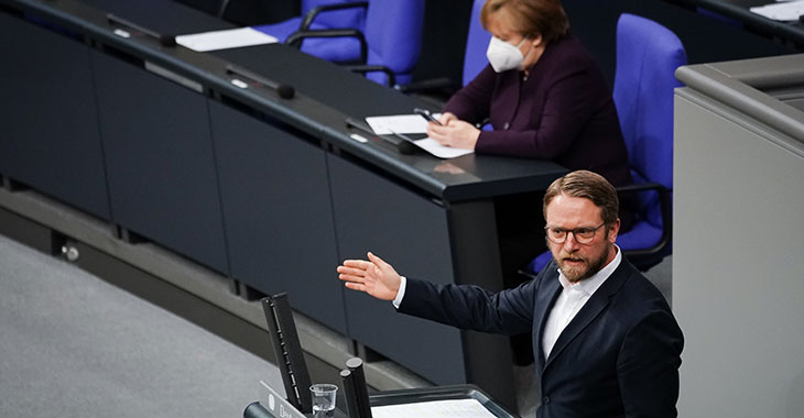 Jan Korte spricht im Plenum mit Angela Merkel im Hintergrund Jan Korte spricht im Plenum mit Angela Merkel im Hintergrund