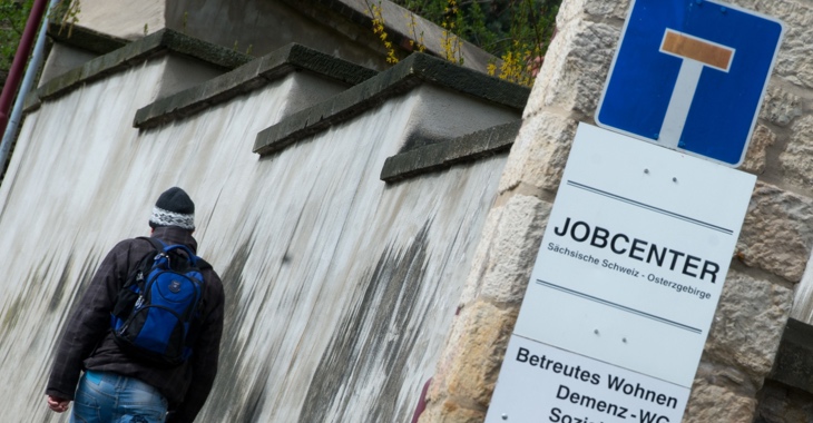 Ein Mann läuft an einem Sackgassen-Schild, das über einem Jobcenter-Schild angebracht ist, vorbei © Arno Burgi/dpa Ein Mann läuft an einem Sackgassen-Schild, das über einem Jobcenter-Schild angebracht ist, vorbei © Arno Burgi/dpa