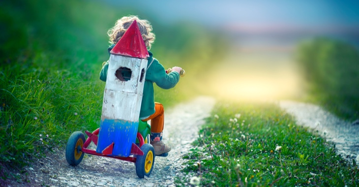 Ein Kind fährt mit einem Dreirad auf einen Feldweg mit einer aus Pappe gebastelten Weltraum-Rakete auf den Rück geschnallt © iStock/oops7 Ein Kind fährt mit einem Dreirad auf einen Feldweg mit einer aus Pappe gebastelten Weltraum-Rakete auf den Rück geschnallt © iStock/oops7