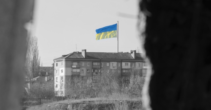 Blick durch ein Fenster eines zerstörten Hauses auf die ukrainische Flagge auf einem gegenüberliegenden Haus © iStock/Ihor Martsenyuk Blick durch ein Fenster eines zerstörten Hauses auf die ukrainische Flagge auf einem gegenüberliegenden Haus © iStock/Ihor Martsenyuk