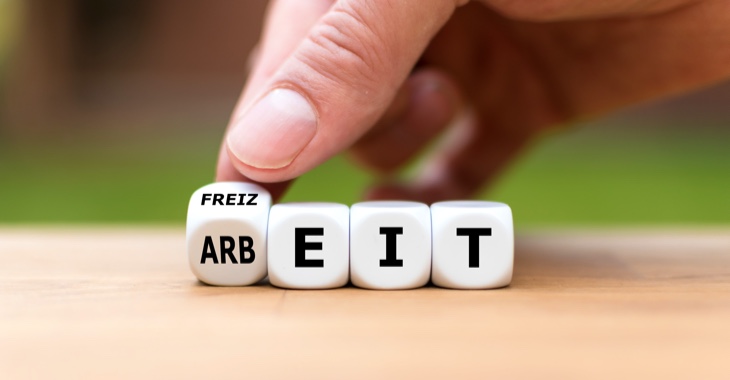 Eine Hand auf vier Würfel, die die Wörter Arbeit und Freizeit bilden © iStock/Fokusiert