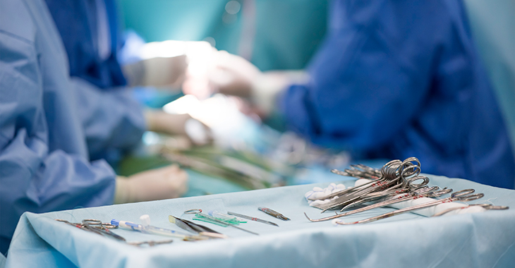Medizinische Instrumente auf einem Tablett in einem Operationssaal, im Hintergrund Ärzte bei einer Operation © iStock/faustasyan