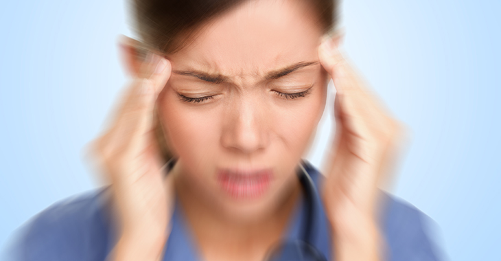 Stress Frau Arbeit Pflege Frau in blauem Hemd fasst sich mit den Fingern beider Hände an die Schläfen und zieht mit geschlossenen Augen die Augenbrauen zusammen. | © iStockphoto.com/Maridav