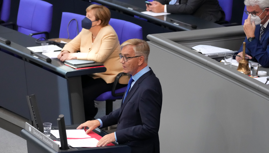 Dietmar Bartsch am Rednerpult des Bundestag, dahinter Bundeskanzlerin Merkel mit Maske auf der Regierungsbank