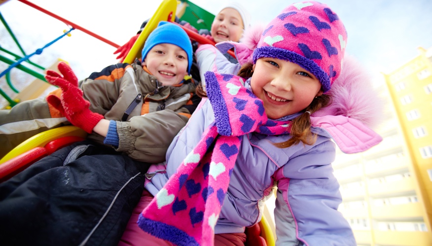Drei Kinder im Winter auf einem Spielplatz © iStock/shironosov